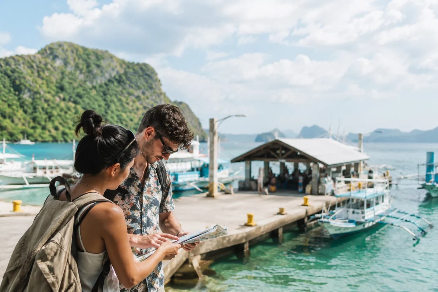 Travelers reviewing a map beside a tropical Philippines harbor