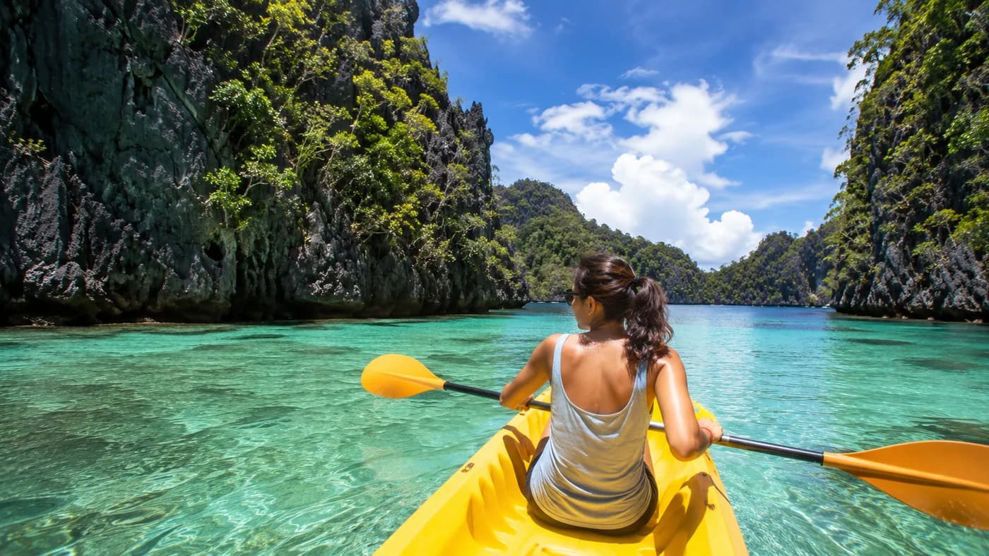 Traveler kayaking through clear tropical water between limestone cliffs